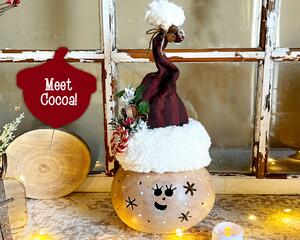 This is a whimsical Christmas elf made with a real dried gourd. This elf's name is Cocoa. Her face is carved into the round gourd shell. 